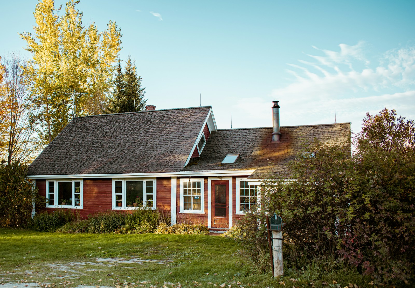 Modest red New England home surrounded by autumn trees